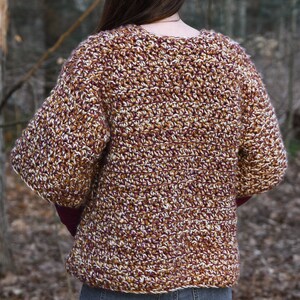 May include: A brown, white, and burgundy crocheted cardigan with a v-neck and long sleeves.