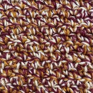 May include: Close-up of a crocheted fabric with a textured pattern in shades of burgundy, white, and gold.