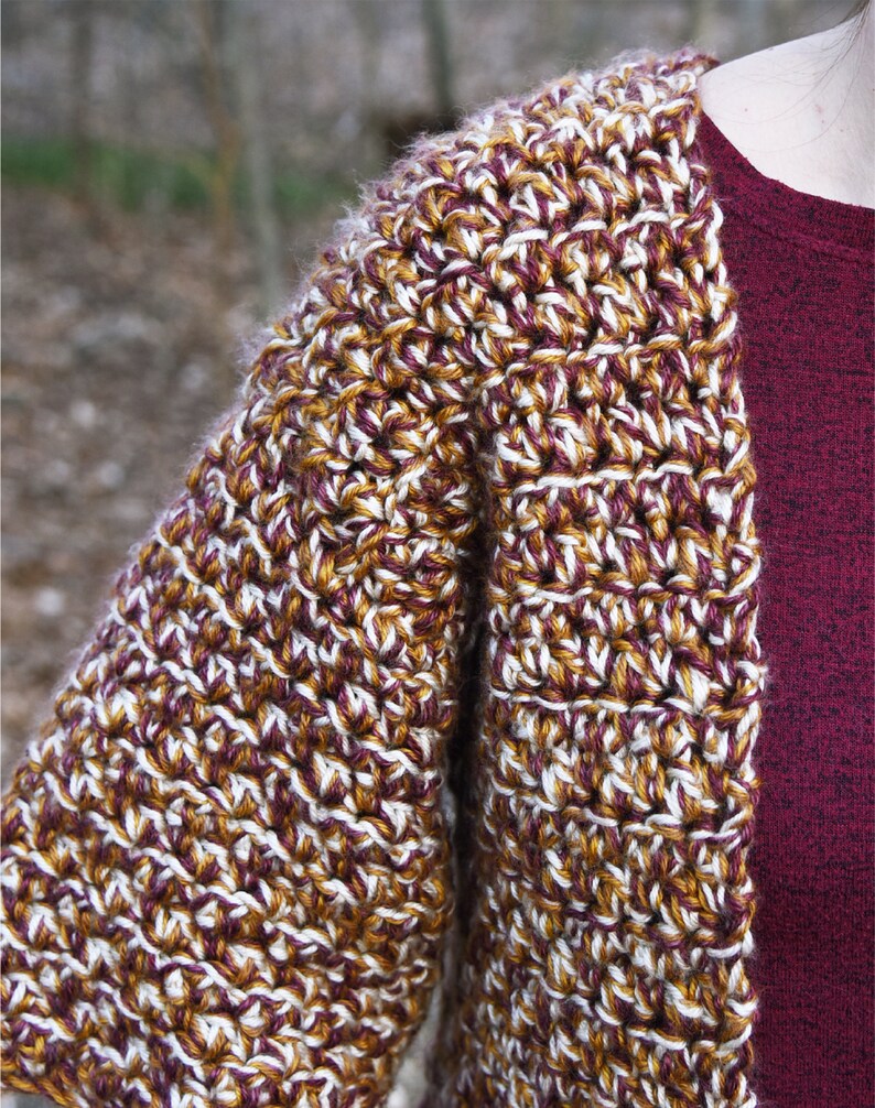 May include: A crocheted cardigan with a brown, white, and burgundy color pattern. The cardigan has a loose fit and a shawl collar.