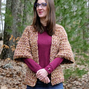 May include: A woman wearing a brown and gold crochet cardigan with a burgundy long-sleeved shirt and blue jeans.