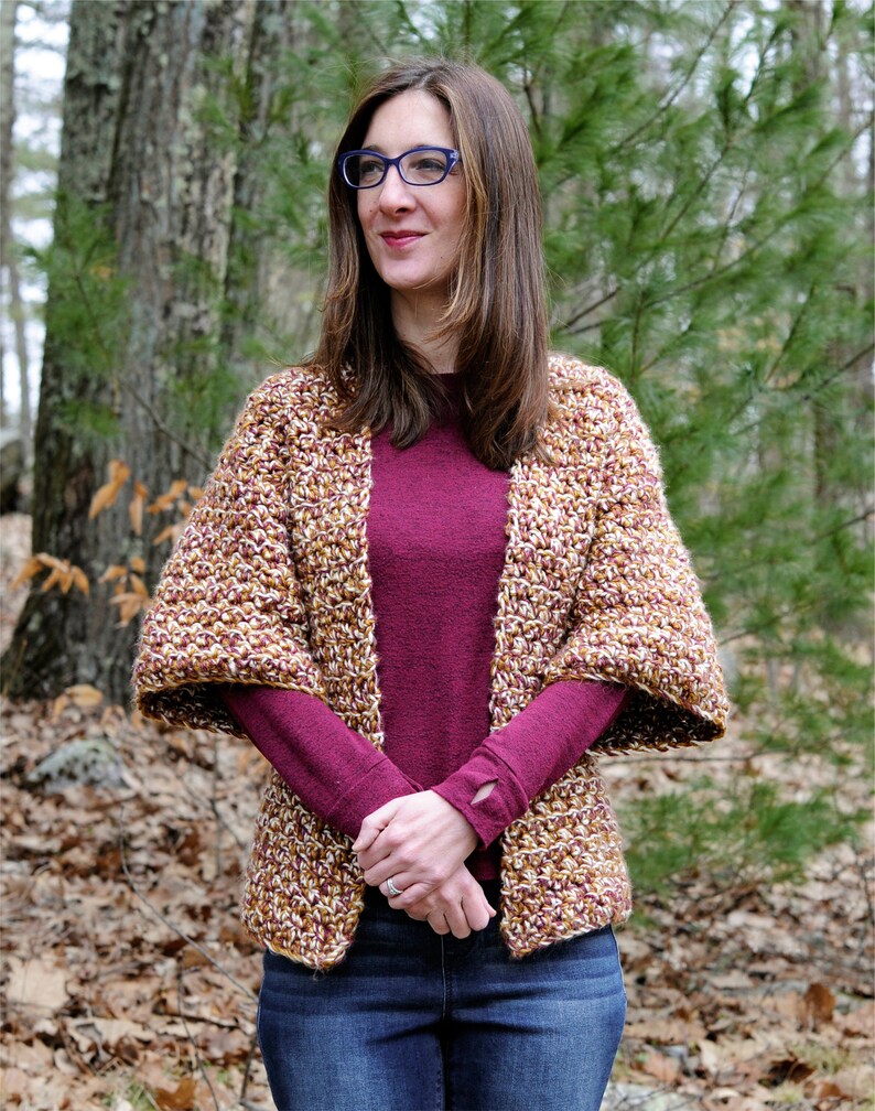 May include: A woman wearing a brown and gold crochet cardigan with a burgundy long-sleeved shirt and blue jeans.