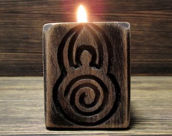 May include: A wooden candle holder with a carved design of a spiral and a circle. The candle is lit and the flame is visible.
