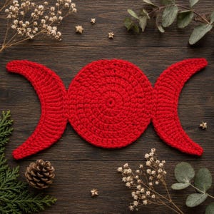 May include: A bright red crochet piece featuring a central circular motif flanked by two crescent moon shapes on either side. The textile item is constructed with a consistent yarn texture and displays a vibrant, solid red color throughout the design.