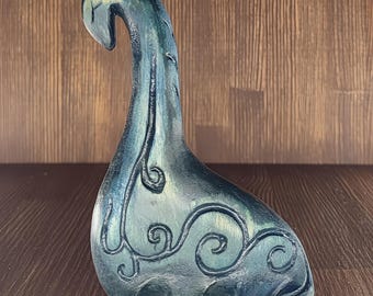 May include: A teal blue wooden sculpture of a mythical sea creature with intricate carved details. The sculpture has a long neck and a curled tail.
