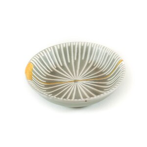 May include: A small, gray ceramic bowl with a white and gold geometric pattern. The bowl has a rounded shape and a slightly flared rim.