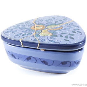 May include: A blue and gold ceramic heart-shaped trinket box with a floral design. The lid has a crack running through it, which is highlighted with gold paint.