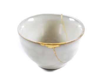 Light gray bowl repaired with Kintsugi the Japanese art that celebrates imperfections and gives new life to objects.