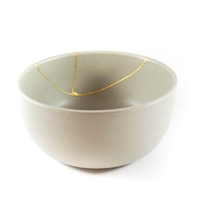 Puede incluir: Un cuenco de cerámica gris claro con un diseño de craquelado dorado. El cuenco es perfecto para servir aperitivos o postres.