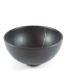 May include: A black bowl with gold cracks. The bowl has a textured, ribbed exterior.