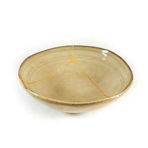 Op de afbeelding: Een kleine, beige keramische kom met een scheur die is gevuld met gouden verf.