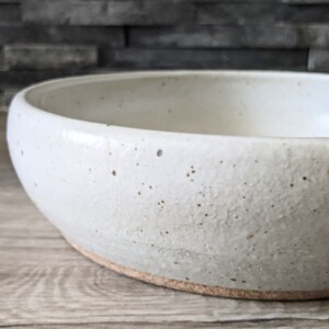 May include: A white ceramic bowl with a speckled glaze. The bowl has a rounded shape and a slightly flared rim.