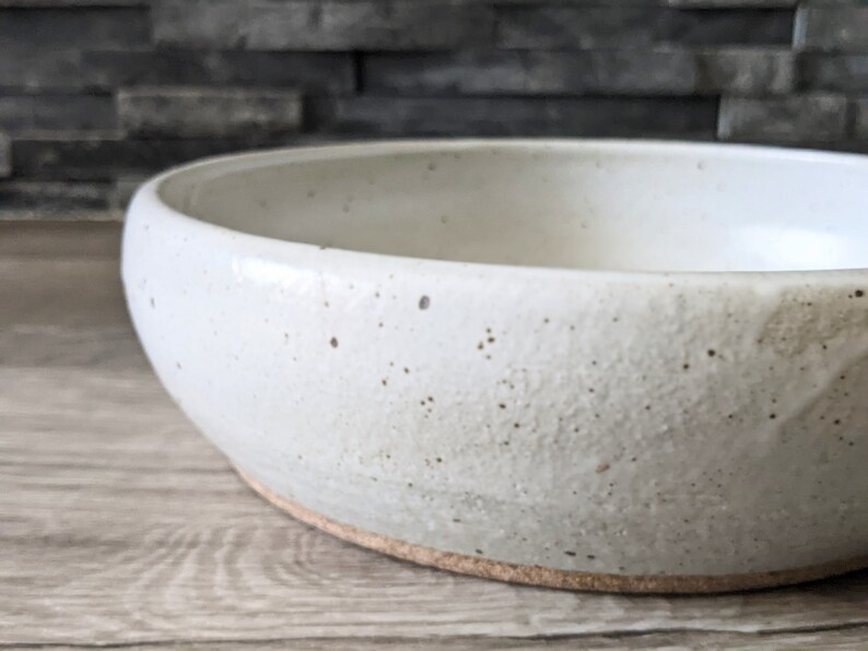 May include: A white ceramic bowl with a speckled glaze. The bowl has a rounded shape and a slightly flared rim.