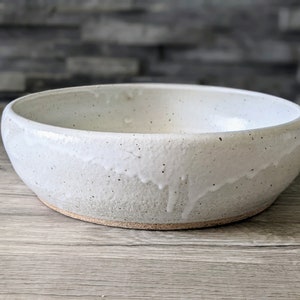 May include: A white ceramic bowl with a speckled glaze. The bowl has a rounded shape and a slightly uneven rim.