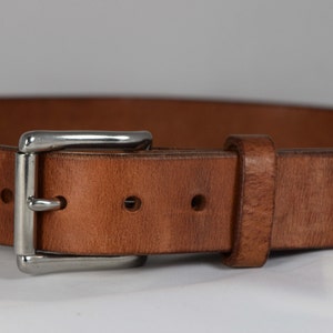May include: A brown leather belt with a silver buckle. The belt has five holes for adjusting the size.
