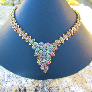 Könnte beinhalten: Eine goldene und schillernde Perlenkette mit einem kaskadierenden Blumendesign. Die Kette wird auf einer schwarzen, kegelförmigen Oberfläche präsentiert.