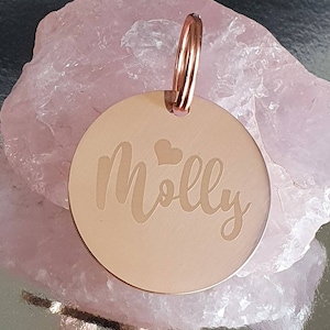 May include: Rose gold pet tag with the name "Molly" engraved in a cursive font and two small hearts above the name.