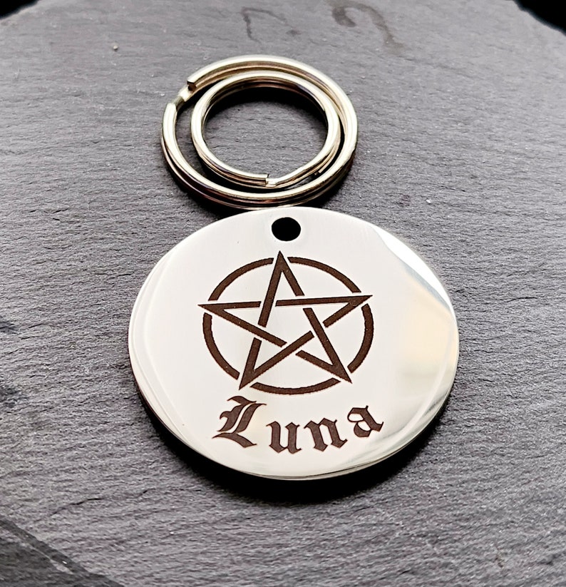 May include: Silver pet tag with a pentagram design and the name "Luna" engraved in a gothic font.