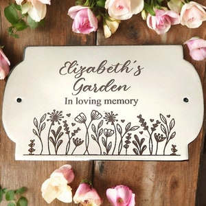 Könnte beinhalten: Weißes Holzschild für den Garten mit schwarzer Aufschrift "Elizabeth's Garden In loving memory". Das Schild hat ein florales Design mit kleinen Herzen.