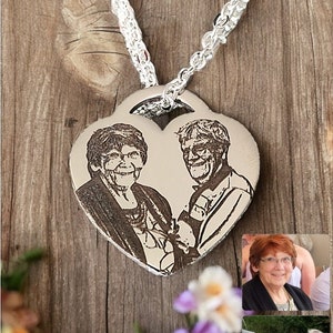 May include: A silver heart-shaped pendant necklace with a black and white engraved image of a couple. The necklace is on a wooden surface with flowers.