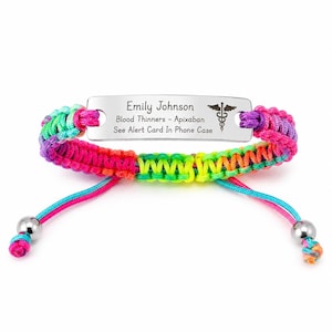 May include: A medical alert bracelet featuring a silver-toned rectangular metal plate engraved with the name Emily Johnson, the text Blood Thinners - Apixaban, See Alert Card In Phone Case, and a caduceus symbol, attached to a multicoloured braided cord.