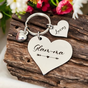 May include: A silver keychain with three heart-shaped charms. One charm is a small, solid heart. The second charm is a heart with the name "Lucas" engraved. The third charm has the word "Glam-ma" and an arrow design.
