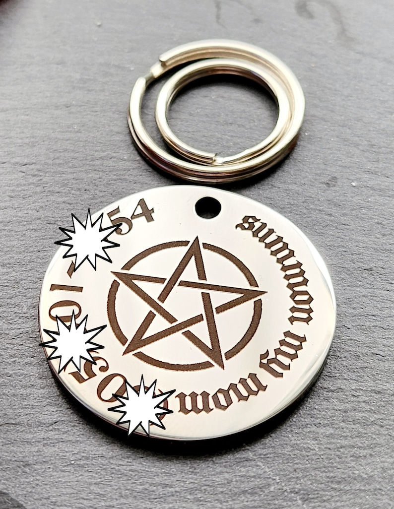 May include: A silver-toned metal keychain with a round tag featuring a pentagram and the text "summon thy demons" in a gothic font. The tag has a hole at the top for attaching to a keyring.