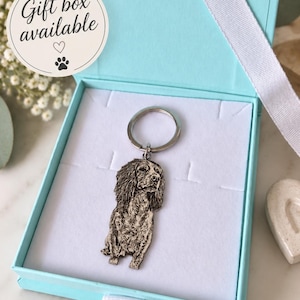 May include: A silver-toned metal keyring featuring a detailed engraved portrait of a long-eared dog, presented inside a light blue gift box with a white ribbon. A circular sticker on the box lid displays the text Gift box available with a heart and paw print.