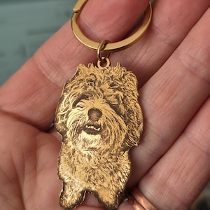 May include: A gold-toned metal keyring featuring a custom laser-engraved portrait of a shaggy-haired dog. The pendant is shaped to the outline of the dog's head and upper body, attached to a circular split ring for keys.