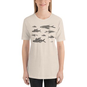 May include: A beige t-shirt with a black and white illustration of a school of flying fish.