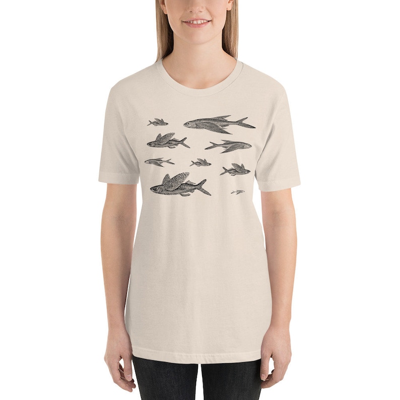 May include: A beige t-shirt with a black and white illustration of a school of flying fish.