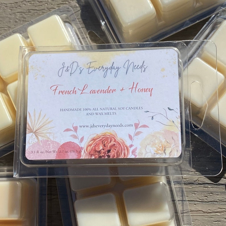 May include: A package of six soy wax melts in a clear plastic container. The label reads "J&D's Everyday Needs French Lavender + Honey Handmade 100% All Natural Soy Candles and Wax Melts www.jdseverydayneeds.com 3.1 fl. oz./Net Wt 2.7 oz. (76.5 g".