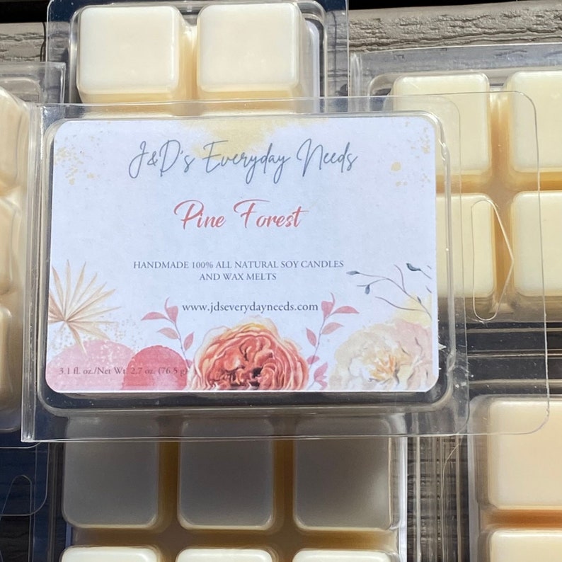 May include: A pack of six soy wax melts in a clear plastic container. The label reads "J&D's Everyday Needs Pine Forest Handmade 100% All Natural Soy Candles and Wax Melts www.jdseverydayneeds.com 3.1 fl. oz./Net Wt. 2.7 oz (76.5 g)". The label has a floral design with a peach, pink, and white color scheme.