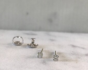 May include: A pair of silver stud earrings with small, clear round gemstones.