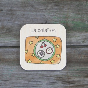 Peut inclure: Une carte en bois avec le texte "La collation" et un dessin d'une assiette avec des cerises, une tranche de pomme et une fleur sur un fond jaune avec des étoiles.