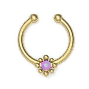 May include: A gold-toned circular septum ring featuring a central round pink opal-like stone surrounded by a cluster of small gold spheres. The hoop is open at the top with two small gold balls at each end, creating a decorative floral-inspired design.
