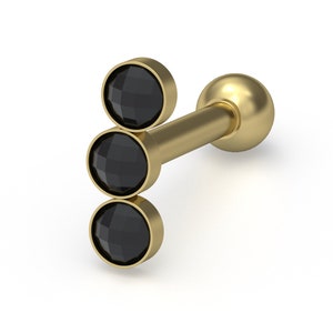 May include: A gold-toned barbell earring featuring a vertical arrangement of three round, faceted black stones set in metal bezels. The post extends from the back of the stone setting and terminates in a smooth, spherical gold-toned ball backing.