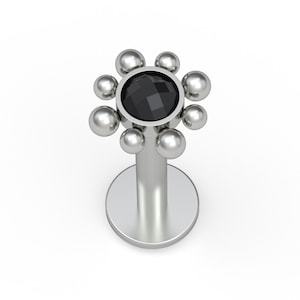 May include: A silver-toned labret stud featuring a circular flat base and a decorative top. The top consists of a central, faceted black gemstone surrounded by a ring of eight small, smooth silver-toned spheres arranged in a flower-like pattern.
