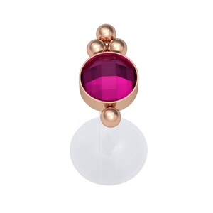 Könnte beinhalten: Ein Körperschmuck-Stecker aus Roségold mit einem runden, facettierten dunkelrosa Edelstein in einer Metallfassung. Das Design umfasst drei kleine Roségoldkugeln über dem Stein und eine Kugel darunter, befestigt an einer transparenten, flachen Basis.