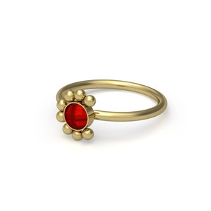 May include: A gold ring featuring a central circular red gemstone. The setting is surrounded by a series of small, smooth gold spheres arranged in a sunburst pattern, attached to a plain, thin, polished gold band.