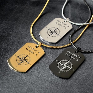 Könnte beinhalten: Drei Halsketten im Dog-Tag-Stil in Gold, Silber und Schwarz. Jedes Tag hat ein Kompassrosen-Design und die Koordinaten 52.5200° N 13.4050° E. Die Halsketten haben passende Ketten.