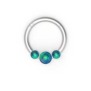 以下が含まれることがあります： 3つの虹色の緑色のオパールのような石が付いたシルバーのフープ。フープはボディピアスのジュエリーです。