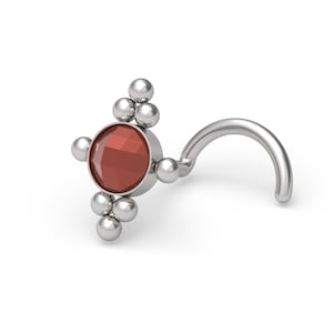 May include: A silver-toned nose stud featuring a central circular red faceted gemstone. The setting is accented with a cluster of three small polished silver spheres at the top and bottom, and a single sphere on the left side, attached to a curved post.