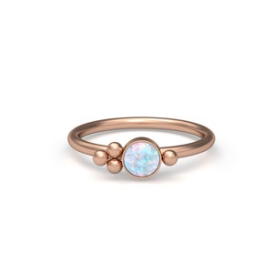 Può includere: Un anello in oro rosa con un gruppo di piccole perle e una pietra preziosa rotonda di opale al centro.