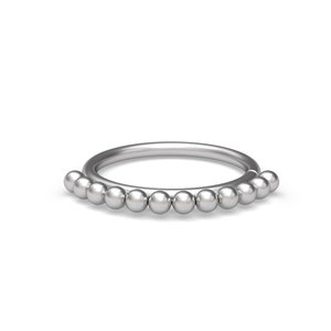Puede incluir: Un anillo circular de tono plateado que presenta una serie de pequeñas esferas metálicas uniformes fijadas a lo largo del borde exterior de la banda. El diseño consiste en un aro liso y continuo adornado con una fila de cuentas pulidas.