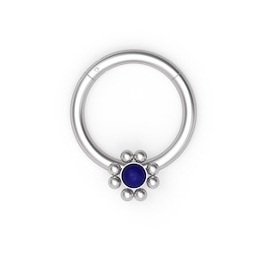 Puede incluir: Anillo de piercing corporal de plata con una gema azul en el centro de un diseño con forma de flor.