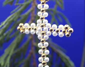 Könnte beinhalten: Ein weißer und goldener Perlenkreuz-Anhänger. Das Kreuz besteht aus kleinen weißen Perlen und goldenen Perlen und hängt an einem goldenen Draht.