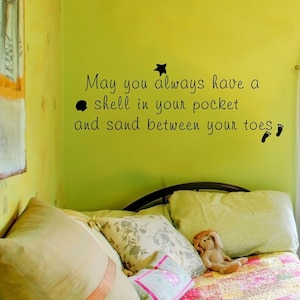 May include: A yellow wall with a black vinyl decal that reads "May you always have a shell in your pocket and sand between your toes". The decal is above a bed with a green blanket and pillows.