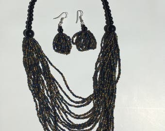 May include: A black beaded necklace with gold accents and matching earrings. The necklace is made of multiple strands of beads and has a tassel-like design.