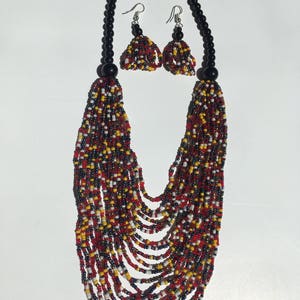 May include: A multi-strand beaded necklace with red, yellow, white, and black beads. The necklace is paired with matching earrings with black beads and silver hooks.