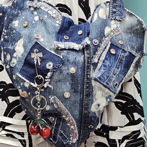 Può includere: Borsa tote in denim a forma di cuore con toppe, strass e un portachiavi a ciliegia. La borsa è realizzata in denim blu strappato con schizzi di vernice bianca. Toppe e abbellimenti aggiungono un tocco decorativo unico.